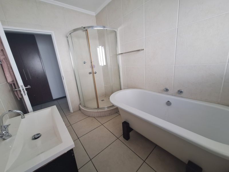 A functional bathroom featuring a freestanding bathtub, a corner shower enclosure, and a vanity basin with neutral wall and floor tiling.