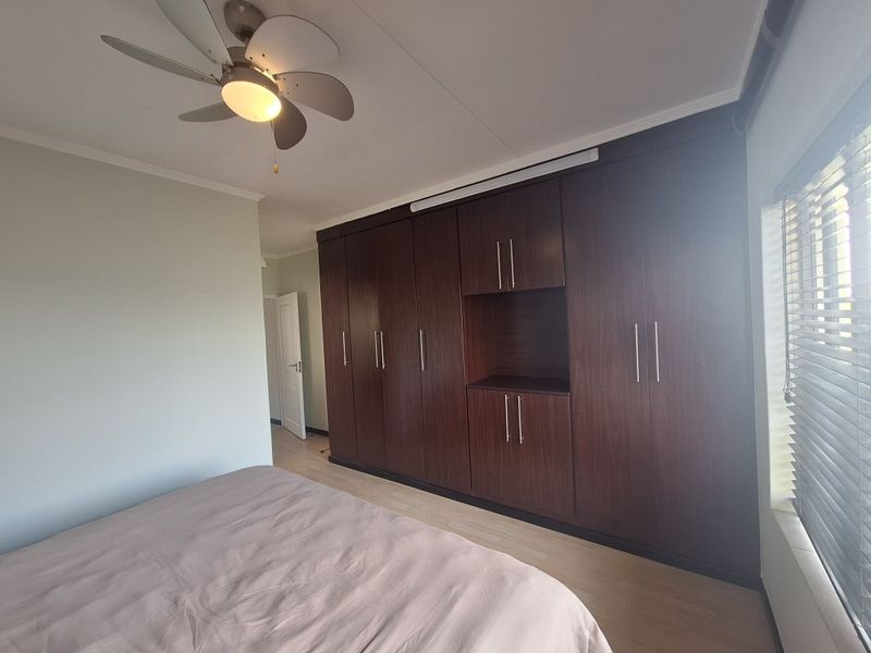 A well-maintained bedroom featuring extensive dark wood built-in cupboards, laminate flooring, a ceiling fan, and venetian blinds.