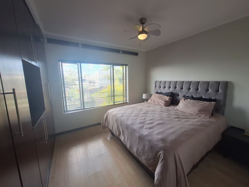 A well-maintained bedroom featuring laminate flooring, built-in cupboards, a ceiling fan, and large windows with venetian blinds.