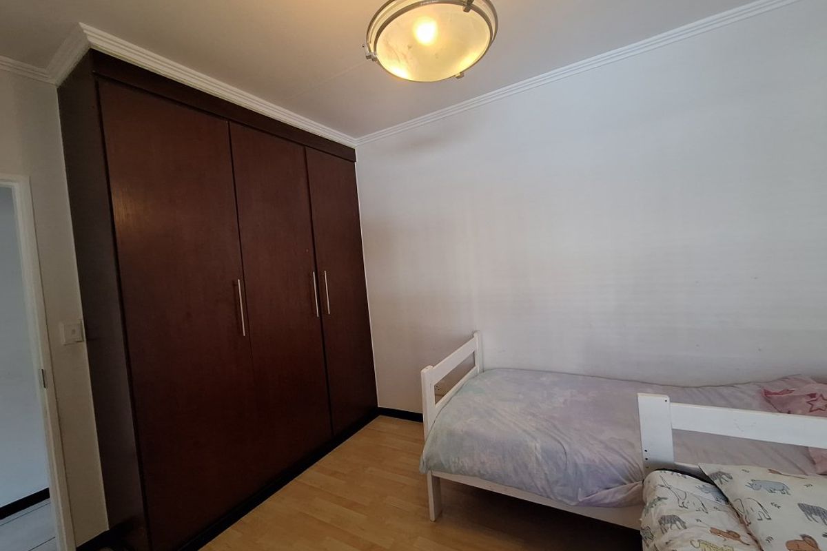 A bedroom featuring laminate flooring, a large dark wood built-in wardrobe, and a central ceiling light fixture.