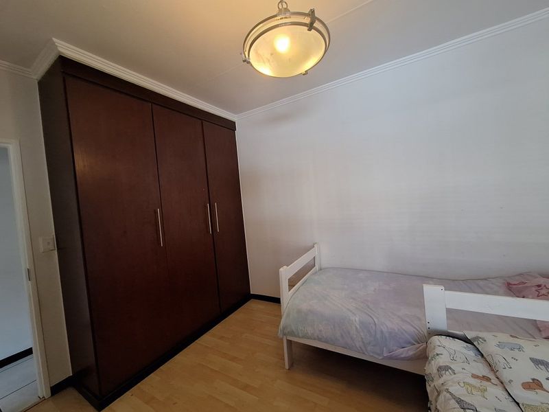 A bedroom featuring laminate flooring, a large dark wood built-in wardrobe, and a central ceiling light fixture.