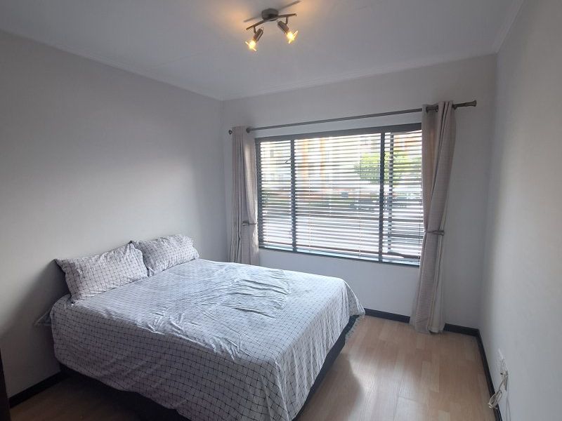 A well-maintained bedroom featuring light-toned laminate flooring, neutral walls, and a ceiling-mounted spotlight fixture, complemented by venetian blinds for privacy.
