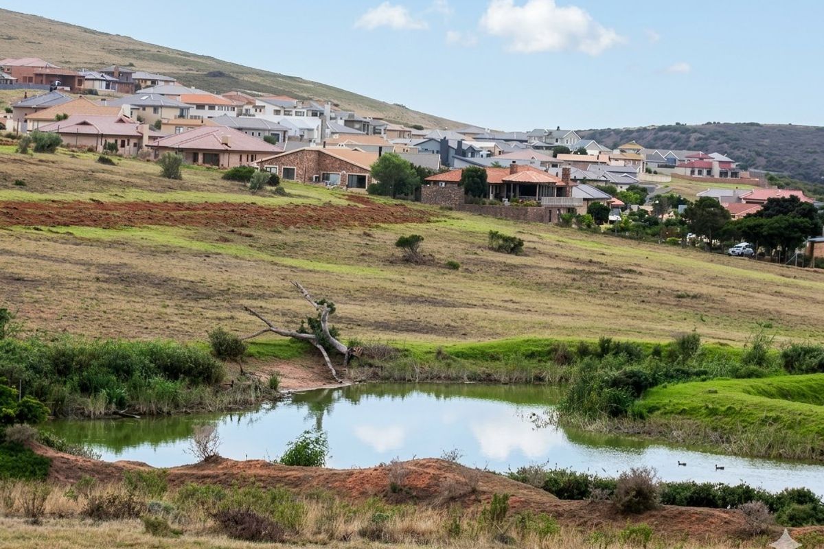 A scenic landscape view overlooking a natural pond with a residential estate nestled on the hillside in the background.
