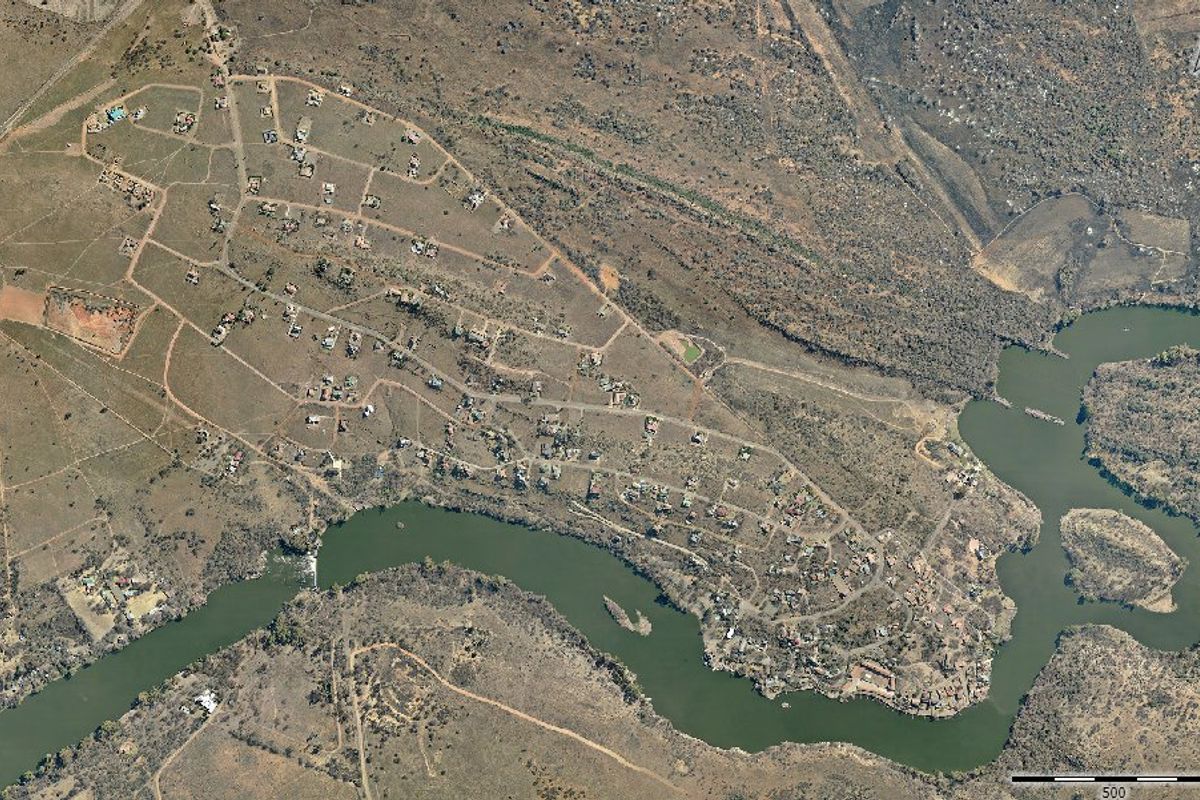 Aerial view of a residential estate situated along a river, showcasing the layout of plots, internal roads, and surrounding natural landscape.