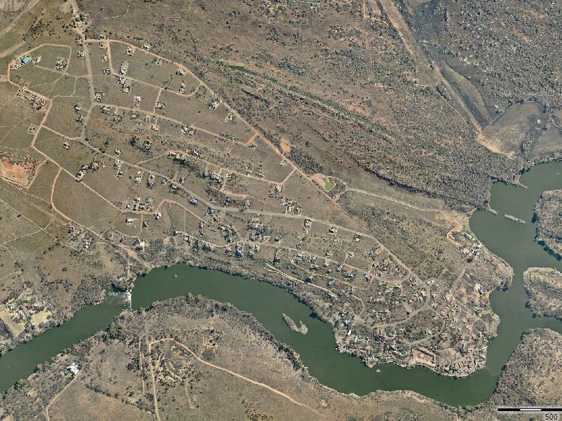 Aerial view of a residential estate situated along a river, showcasing the layout of plots, internal roads, and surrounding natural landscape.