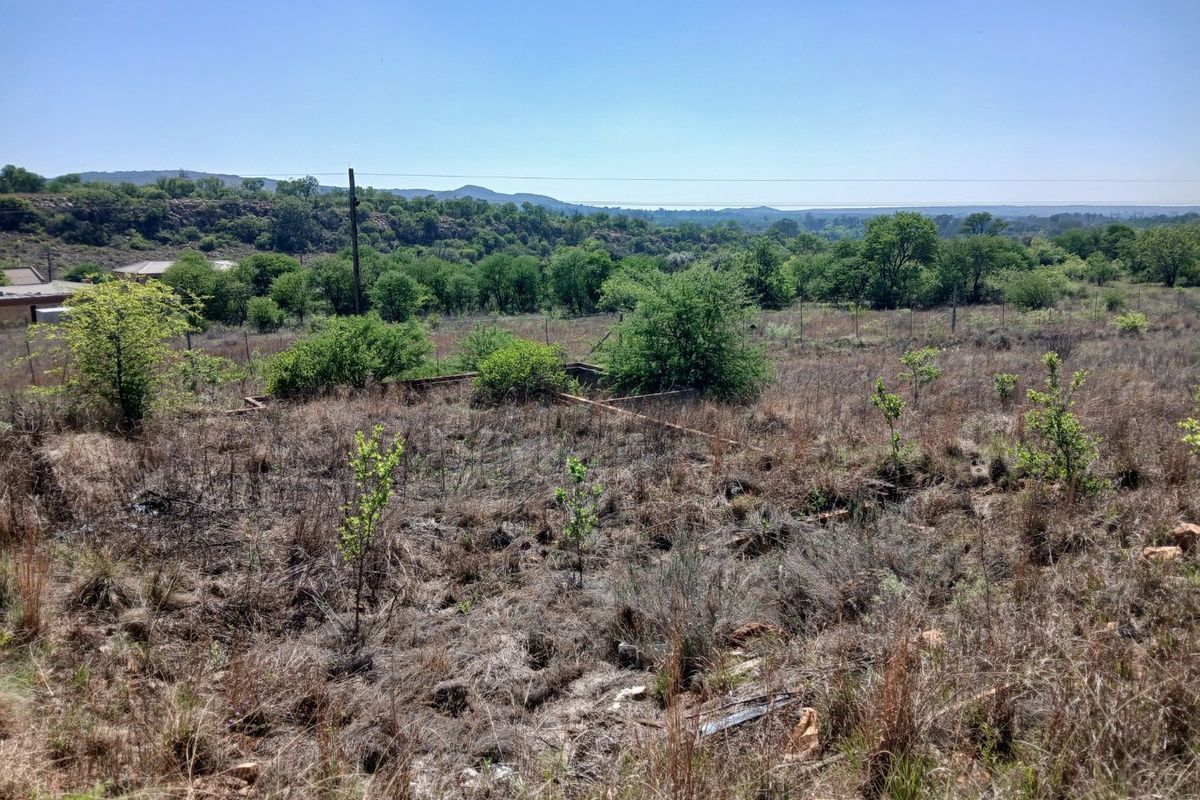 A view of a vacant residential plot featuring natural vegetation, wire fencing, and a utility pole with a scenic landscape backdrop.