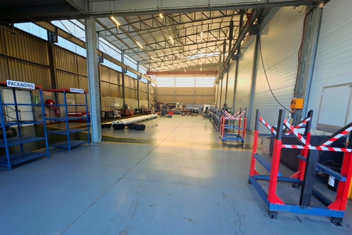 Spacious commercial warehouse or industrial utility space featuring high ceilings, exposed steel trusses, durable epoxy flooring, and functional metal wall cladding.