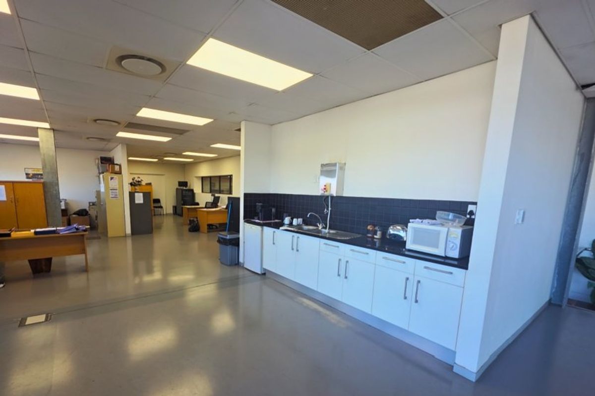 A functional office kitchenette featuring white cabinetry, a dark tiled backsplash, and a sink, integrated into an open-plan commercial workspace.