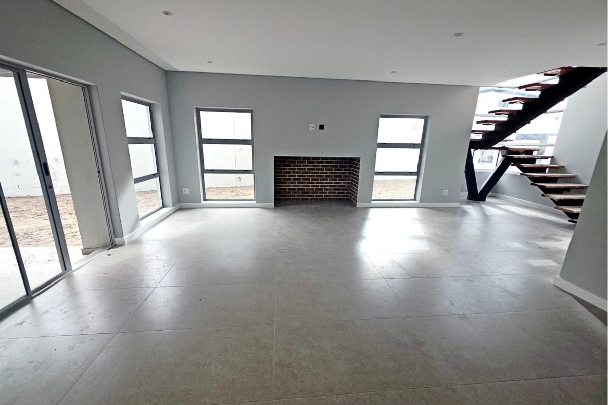 Spacious open-plan living area featuring modern tiled flooring, a brick fireplace, and a contemporary staircase with large windows providing natural light.