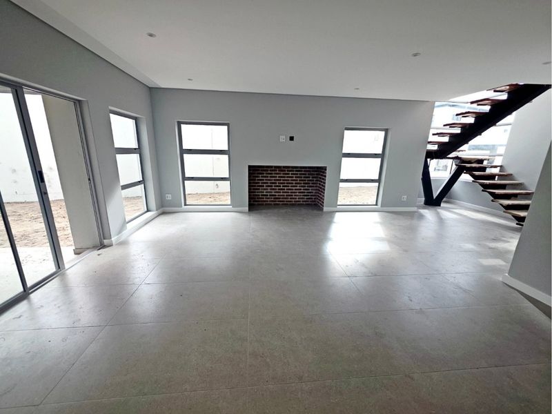 Spacious open-plan living area featuring modern tiled flooring, a brick fireplace, and a contemporary staircase with large windows providing natural light.