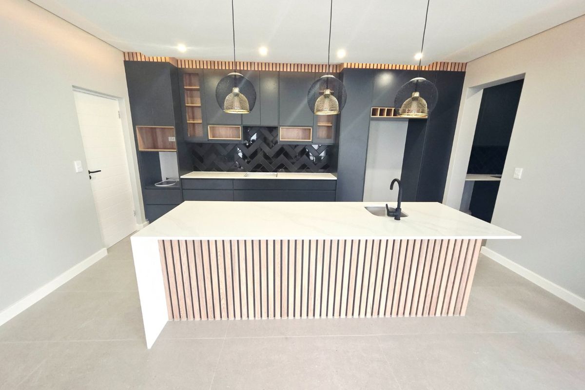 Modern kitchen featuring a central island with stone countertop, dark cabinetry, herringbone backsplash, and contemporary pendant lighting in a clean, open-plan space.