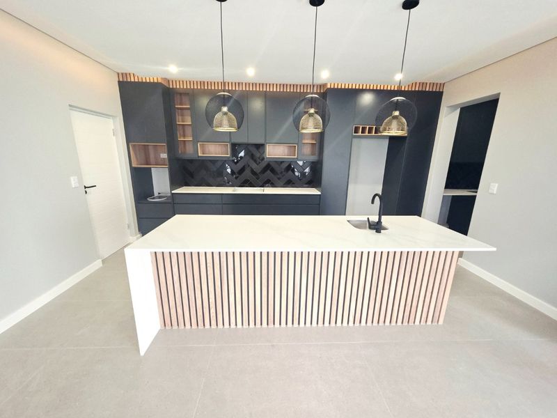 Modern kitchen featuring a central island with stone countertop, dark cabinetry, herringbone backsplash, and contemporary pendant lighting in a clean, open-plan space.