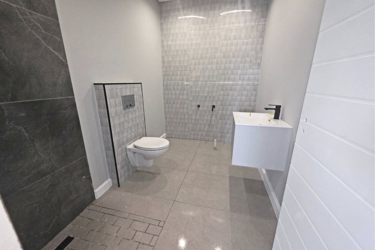 A modern, minimalist bathroom featuring a wall-hung toilet with a concealed cistern, a floating vanity with a black mixer tap, and contemporary tiled finishes.