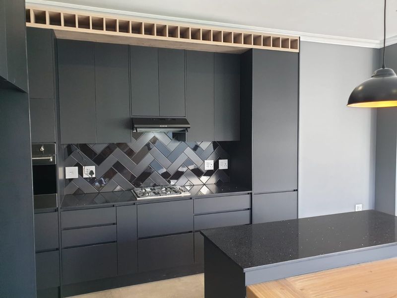 Modern kitchen featuring matte black cabinetry, stone countertops, a gas hob with extractor fan, and a stylish herringbone tile backsplash.