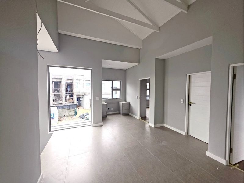 A spacious, light-filled living area featuring high vaulted ceilings, neutral tiled flooring, and modern finishes, currently in a near-complete state.