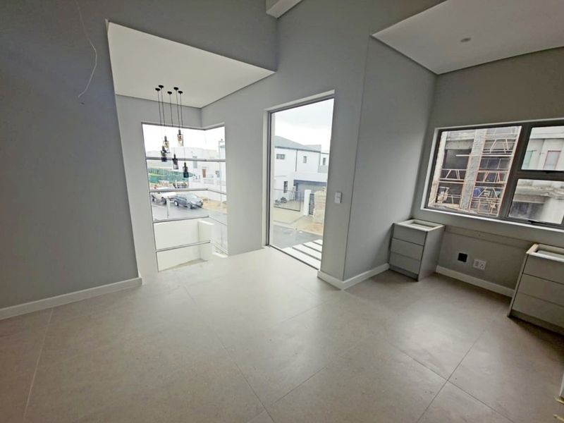A bright, modern, and empty living area featuring large windows, neutral tiled flooring, and contemporary pendant lighting, offering a clean canvas for interior design.