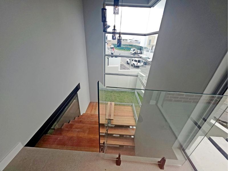Modern staircase featuring timber treads, a frameless glass balustrade, and expansive floor-to-ceiling windows overlooking the street.