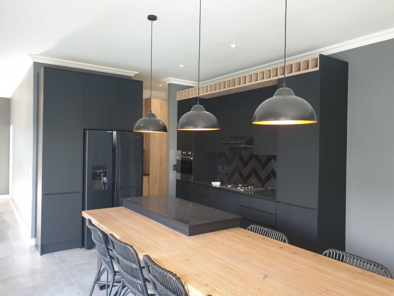 Modern kitchen featuring matte black cabinetry, a stone-topped island with integrated dining space, herringbone backsplash, and high-end built-in appliances.