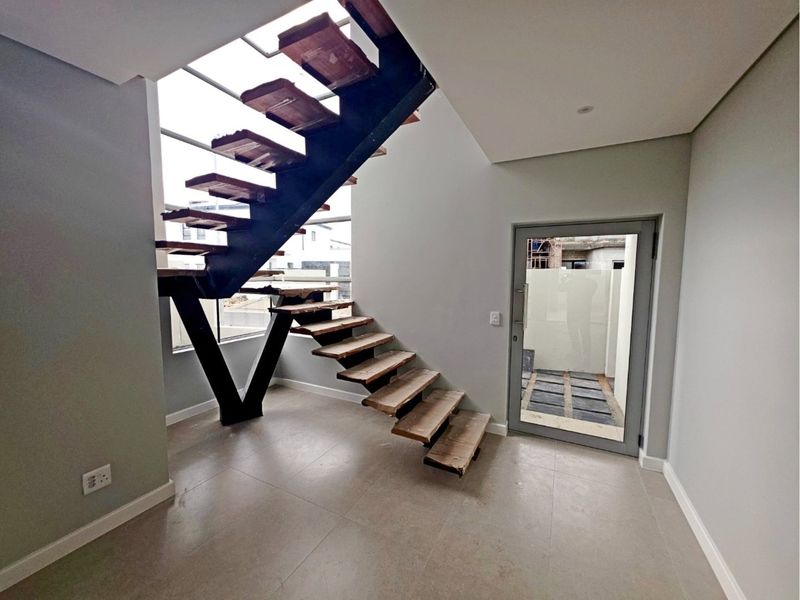 Modern entrance hall featuring a striking floating staircase with timber treads and a steel frame, leading to a glass door with outdoor access.