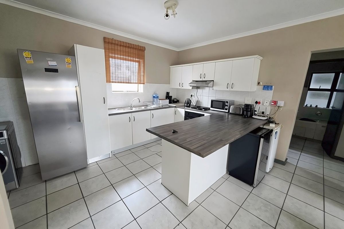 Functional kitchen featuring white cabinetry, dark laminate countertops, tiled flooring, and an integrated extractor fan, offering a practical layout for daily use.