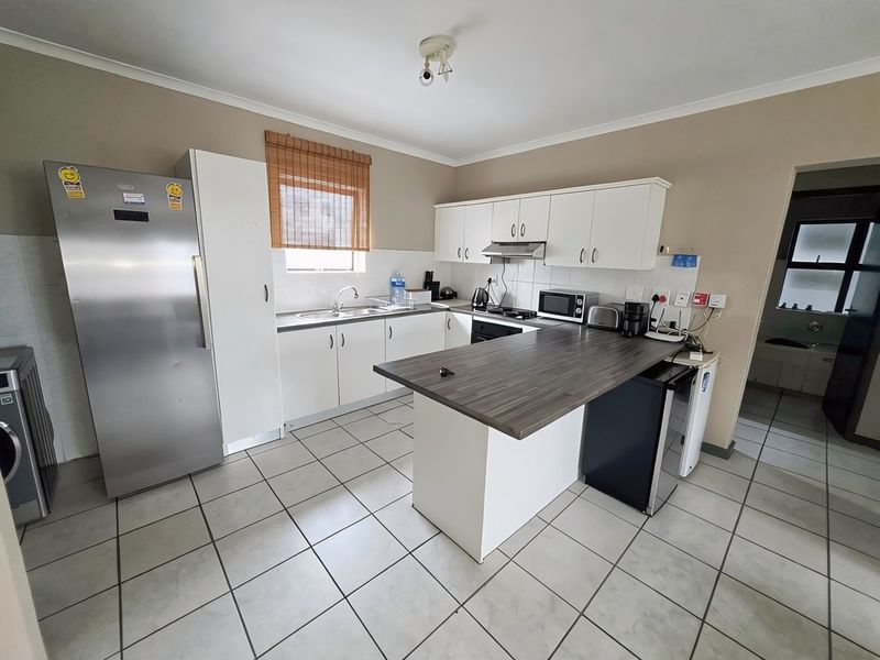Functional kitchen featuring white cabinetry, dark laminate countertops, tiled flooring, and an integrated extractor fan, offering a practical layout for daily use.