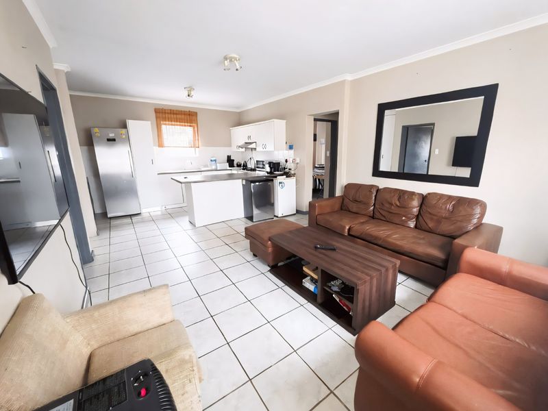 Open-plan living area featuring a functional kitchen with cabinetry and island, seamlessly flowing into a tiled lounge space.