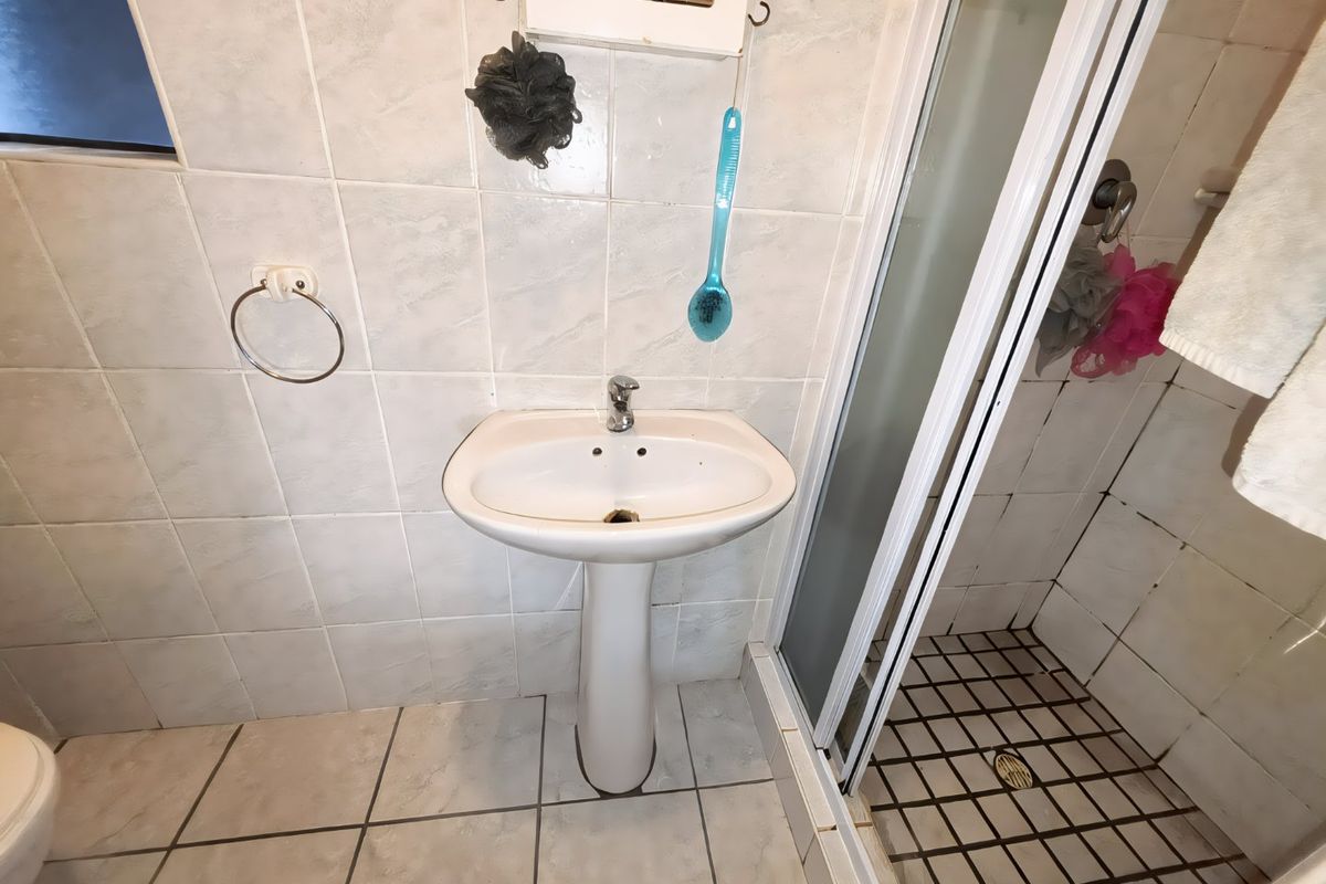 A functional bathroom featuring a pedestal basin, tiled wall and floor finishes, and a separate shower enclosure with a glass door.