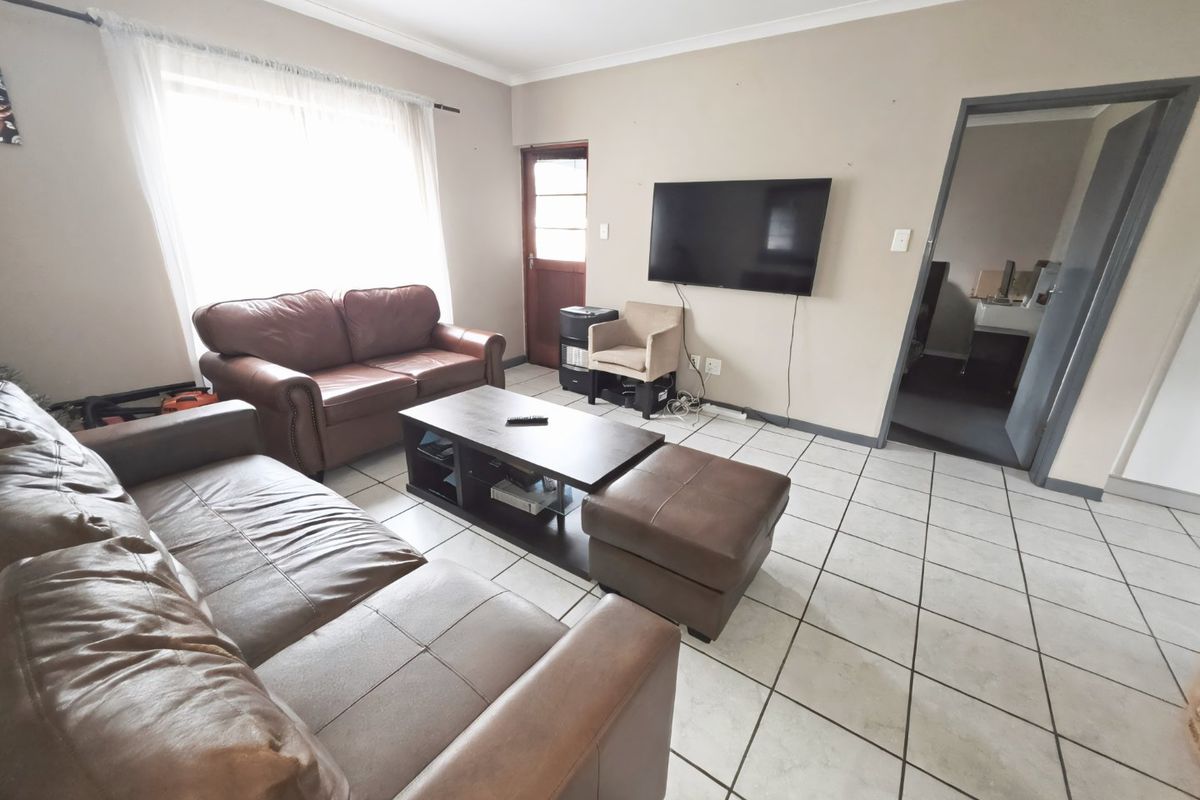 A living room featuring tiled flooring, coved ceilings, and a timber door, providing a functional space with potential for cosmetic updates.