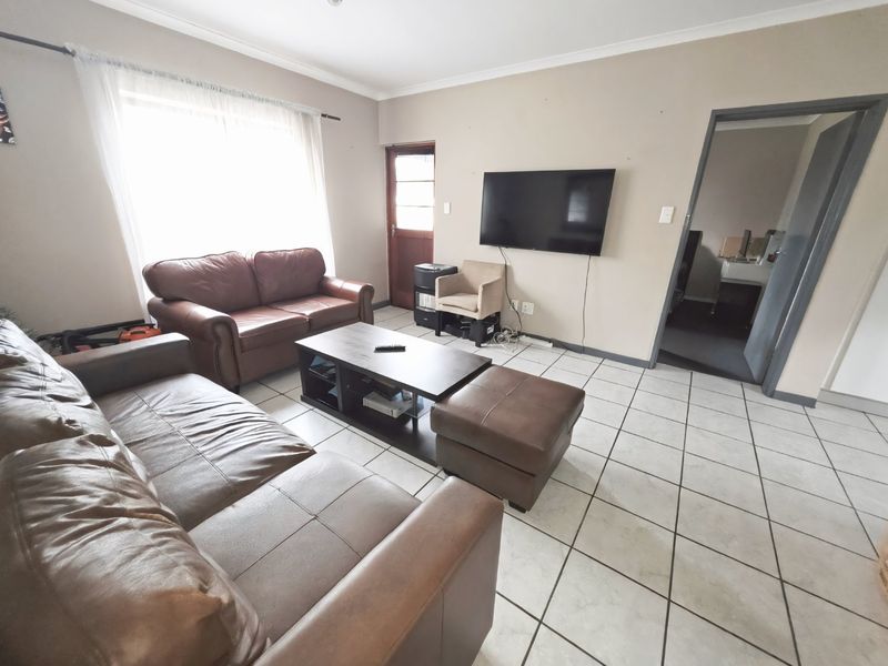 A living room featuring tiled flooring, coved ceilings, and a timber door, providing a functional space with potential for cosmetic updates.