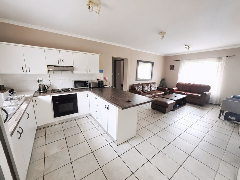 Open-plan living area featuring a functional kitchen with white cabinetry, dark laminate countertops, and tiled flooring throughout the combined kitchen and lounge space.