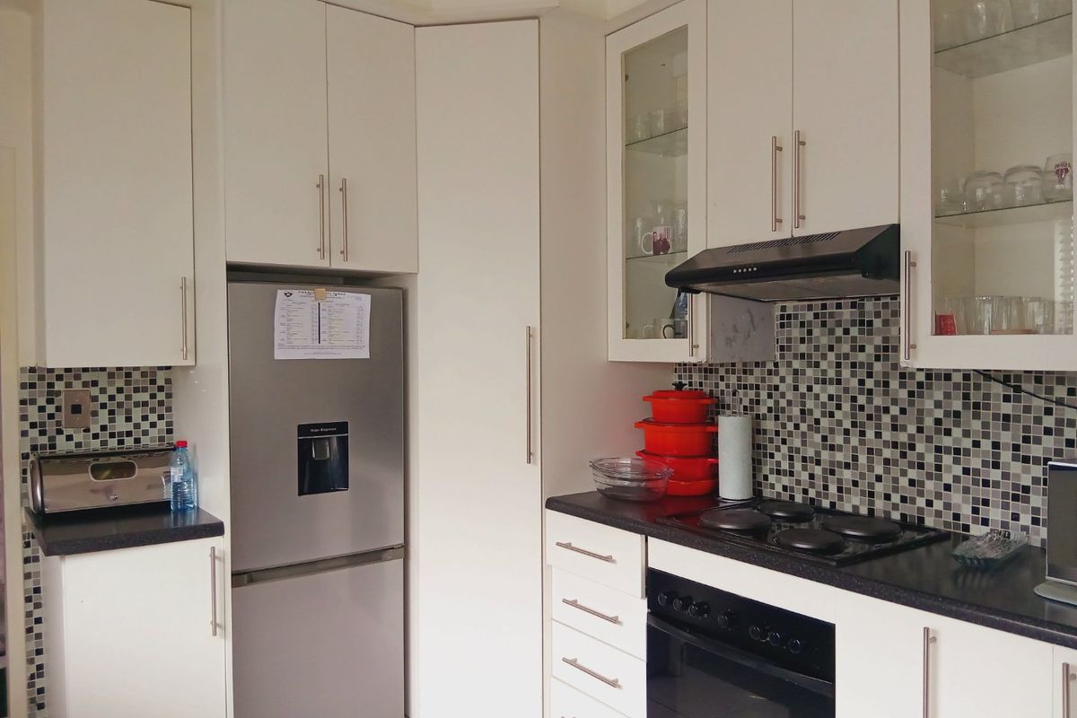 A functional kitchen featuring white cabinetry, mosaic tile backsplash, dark countertops, and integrated appliances including an oven, hob, and extractor fan.