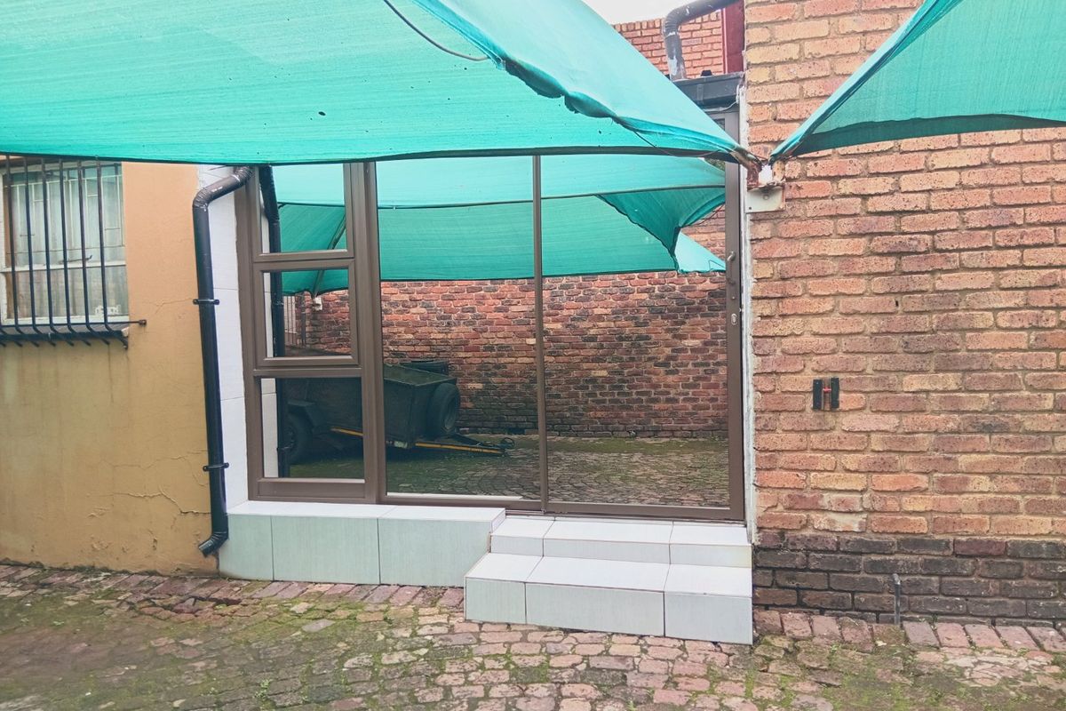 Rear exterior view featuring a sliding glass door, tiled entrance steps, and a shaded courtyard area with cobblestone paving and brick boundary walls.