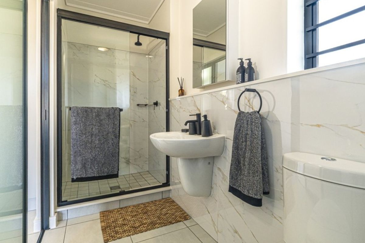 Modern bathroom featuring a glass-enclosed shower, pedestal washbasin, and elegant marble-look wall tiles with contemporary black fixtures.