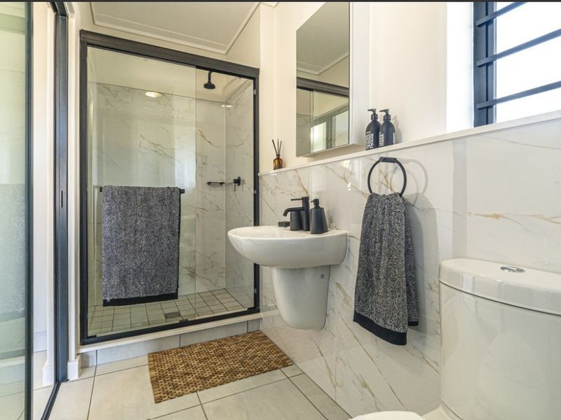 Modern bathroom featuring a glass-enclosed shower, pedestal washbasin, and elegant marble-look wall tiles with contemporary black fixtures.