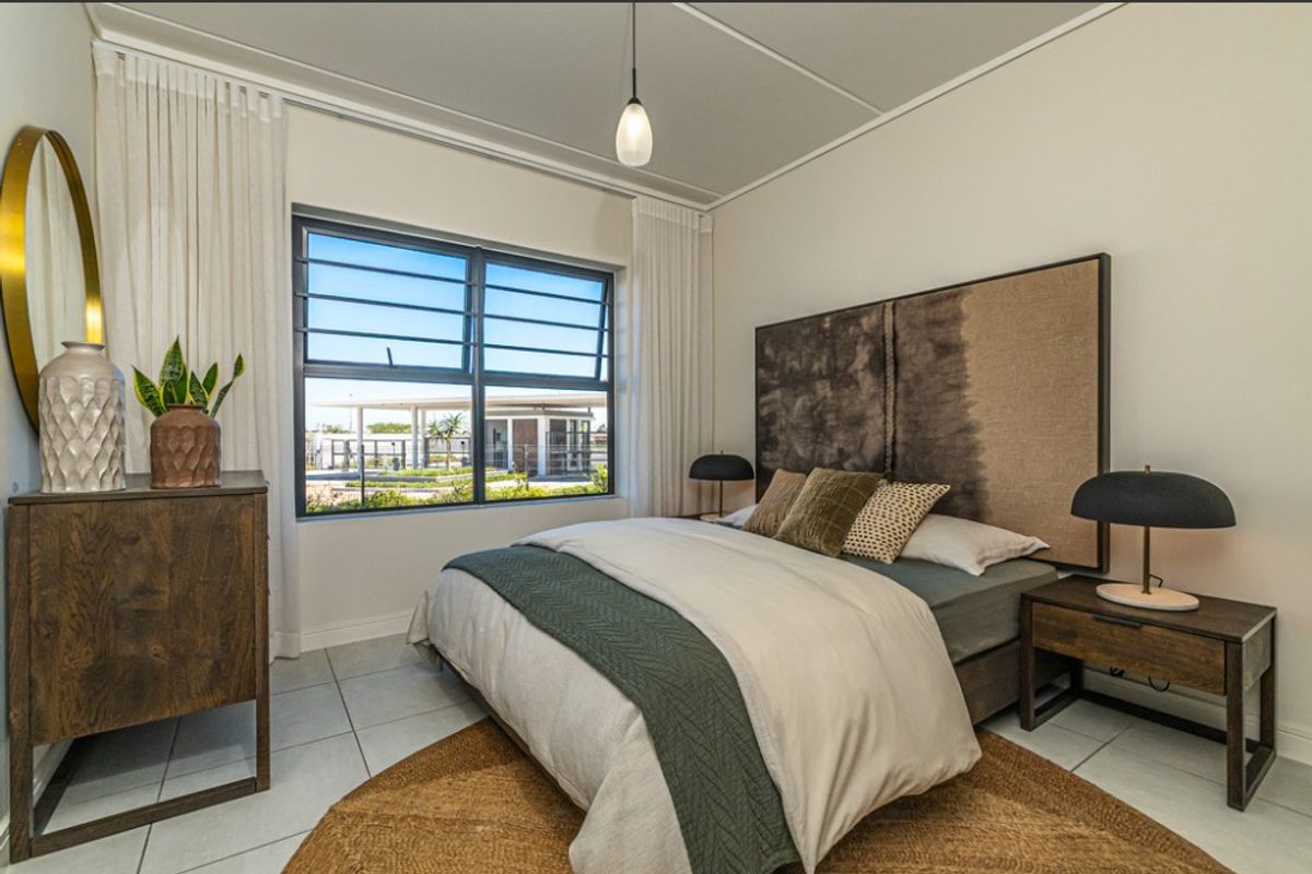 A well-lit bedroom featuring tiled flooring, neutral walls, and a large window with security bars, providing a clean and comfortable living space.