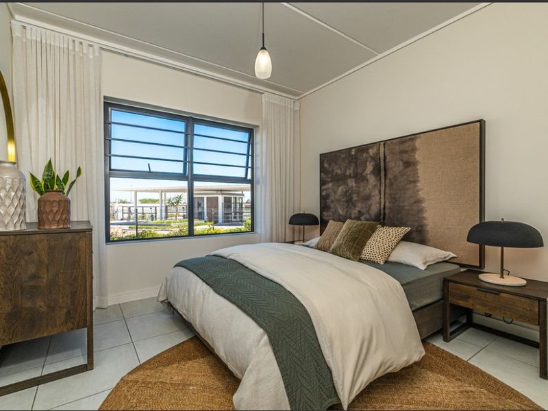 A well-lit bedroom featuring tiled flooring, neutral walls, and a large window with security bars, providing a clean and comfortable living space.