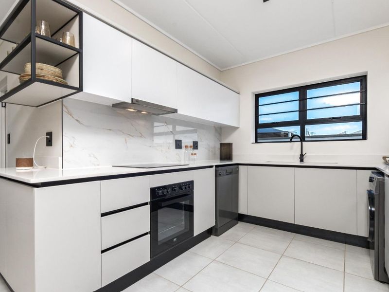 Modern kitchen featuring sleek white cabinetry, marble-look splashback, high-quality black fixtures, integrated appliances, and durable tiled flooring.
