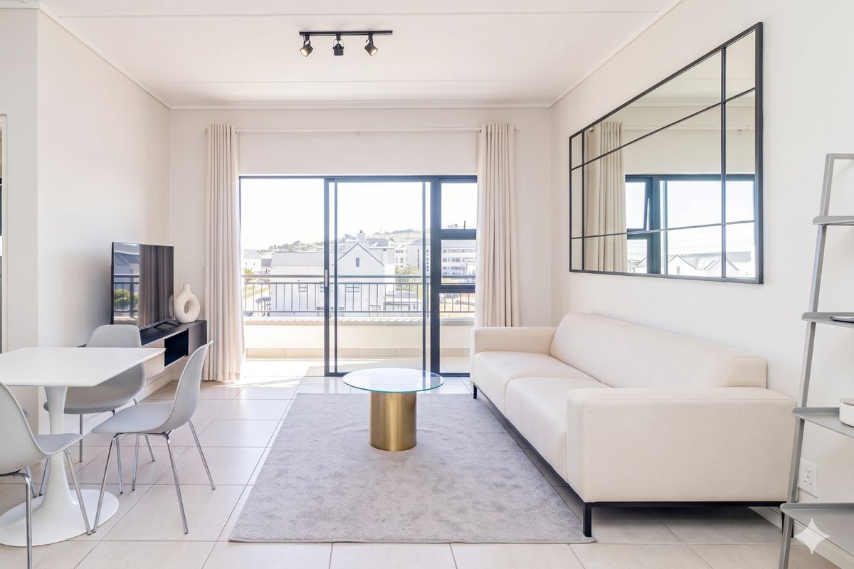 Bright open-plan living area featuring tiled flooring, modern track lighting, and large sliding glass doors leading to a private balcony.
