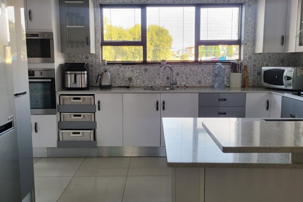 Modern kitchen featuring white and grey cabinetry, stone countertops, built-in appliances, and large format floor tiles with a window overlooking the exterior.