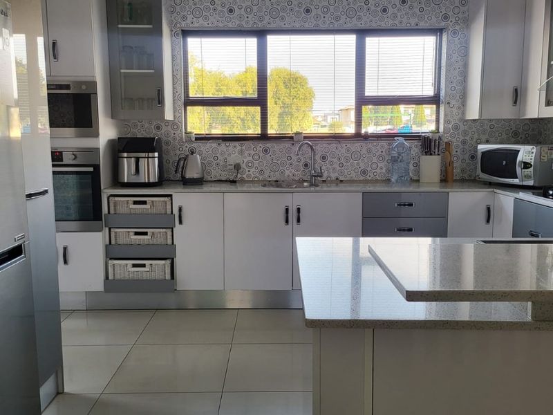 Modern kitchen featuring white and grey cabinetry, stone countertops, built-in appliances, and large format floor tiles with a window overlooking the exterior.