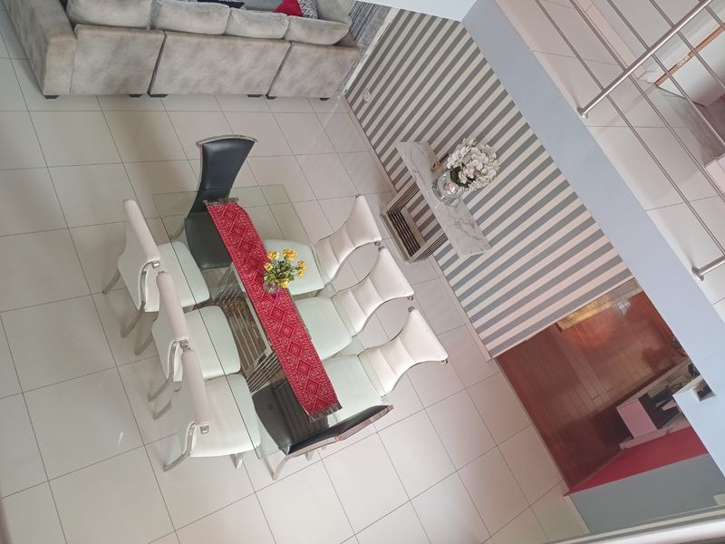 An elevated view of an open-plan living and dining area featuring tiled flooring, a feature striped wall, and a modern staircase railing.