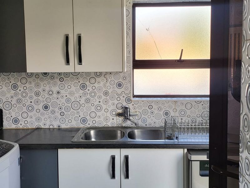 A functional kitchen area featuring built-in cabinetry, a double bowl sink with mixer tap, and patterned tiled backsplash.