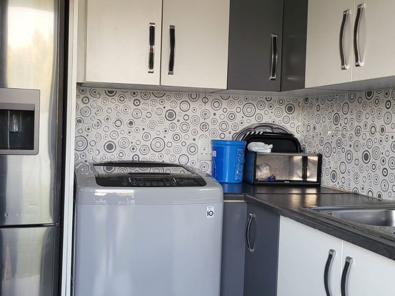 A functional laundry area featuring modern two-tone cabinetry, patterned tile backsplash, and a stainless steel sink integrated into the countertop.