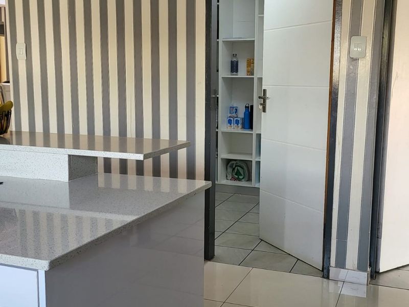 A functional scullery area featuring stone countertops, tiled flooring, and built-in shelving, providing additional storage and prep space adjacent to the main kitchen.