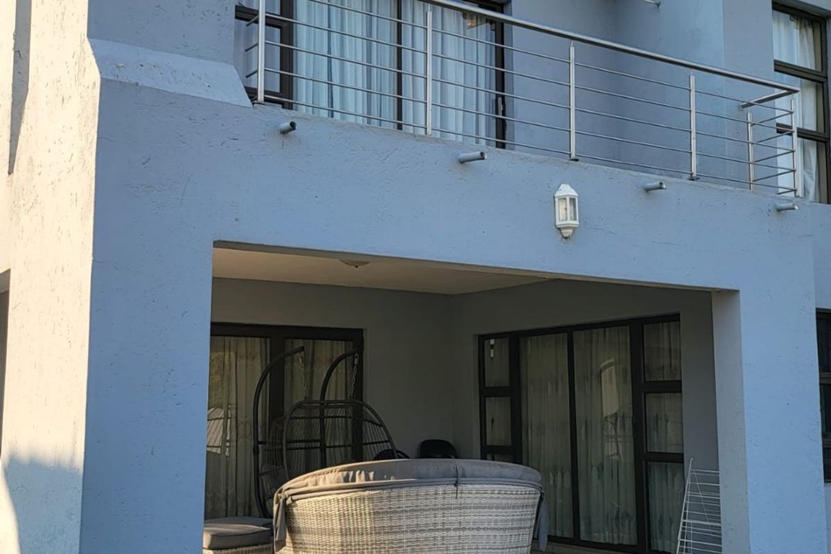 Rear view of the property featuring a covered patio area, tiled flooring, and an upper-level balcony with a stainless steel railing.