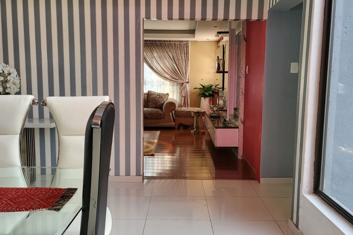 A view from the dining area into the living room, featuring tiled floors, striped wallpaper, and a recessed ceiling design.