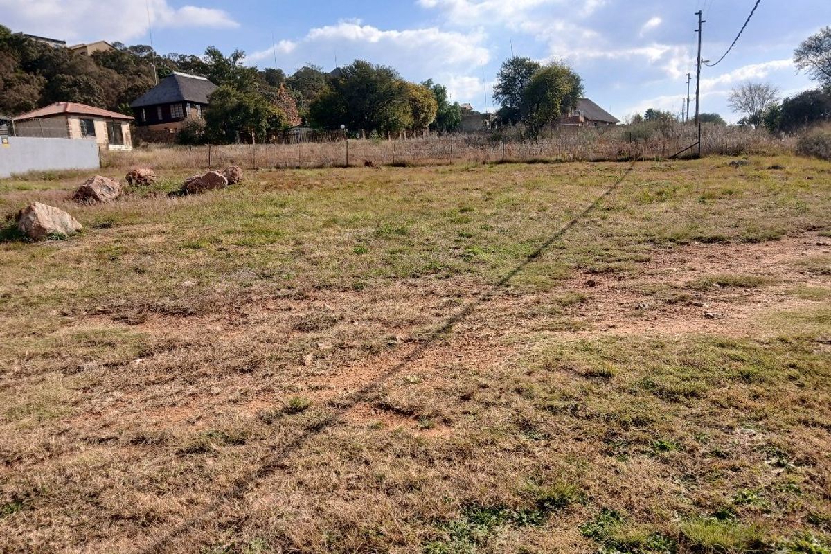 A vacant residential plot featuring natural grass terrain, perimeter fencing, and an existing utility pole on the property boundary.