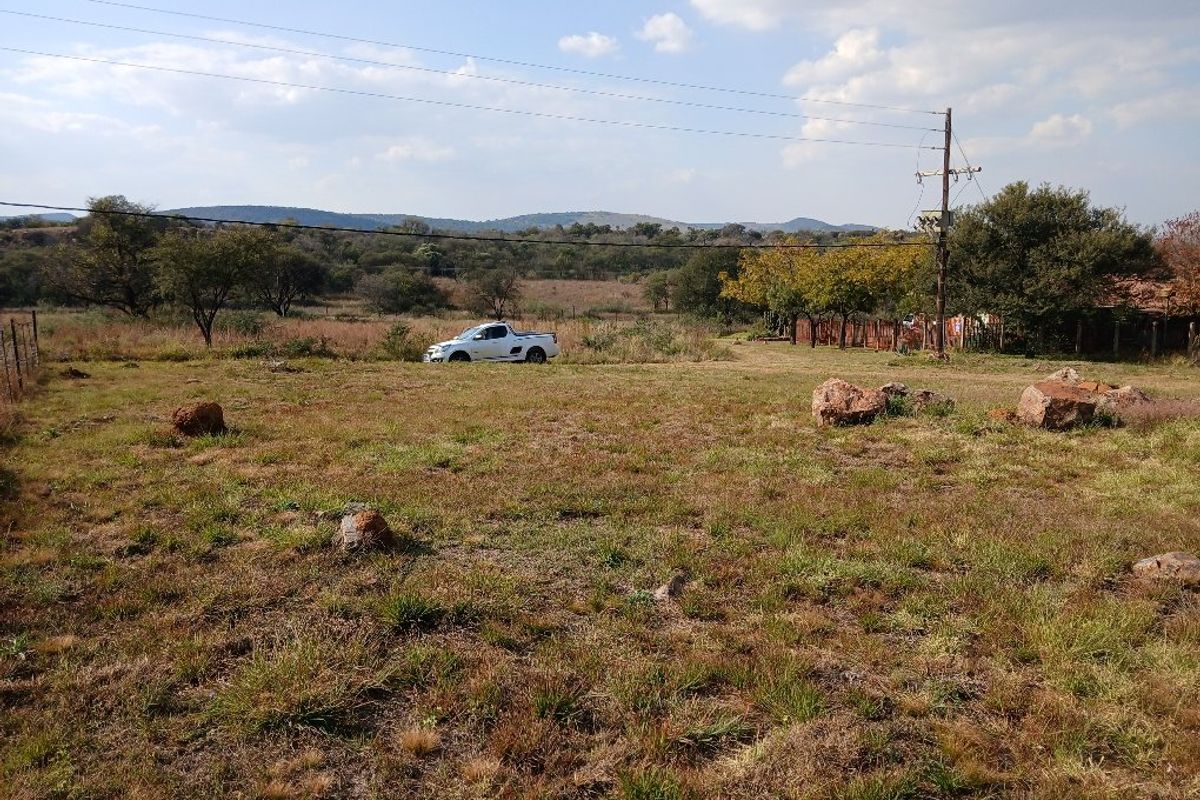 A vacant residential plot featuring natural grass terrain, perimeter fencing, and access to overhead utility infrastructure.