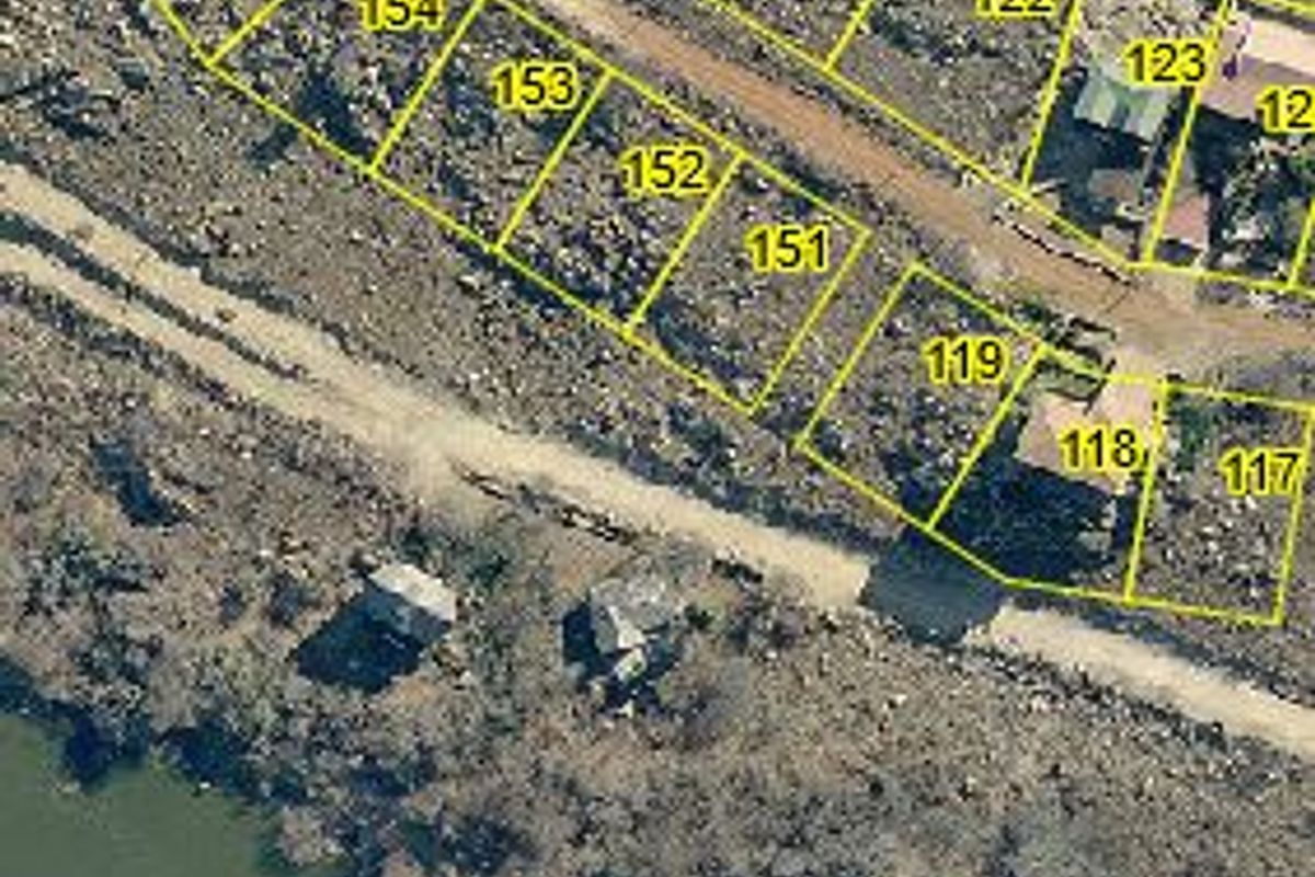 Aerial view of residential vacant land plots situated along a waterfront, featuring unpaved road access and natural terrain.