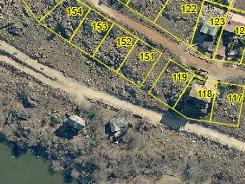 Aerial view of residential vacant land plots situated along a waterfront, featuring unpaved road access and natural terrain.